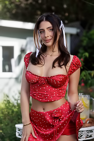 Tru Kait in red polka dot lingerie poses outdoors with tulips and lemonade on white furniture